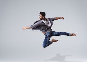 A male contemporary dancer in casual wear leaping gracefully in mid-air, showcasing agility and flexibility.